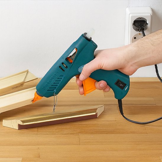 pistolet à colle tenu au-dessus d’une pièce de bois sur une table