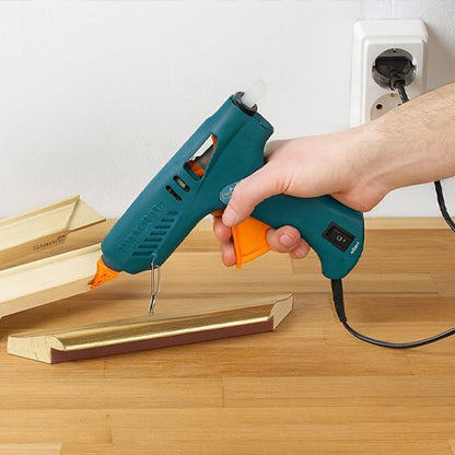 pistolet à colle tenu au-dessus d’une pièce de bois sur une table