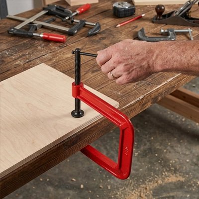 serre joint rouge fixant un panneau sur un établi en bois